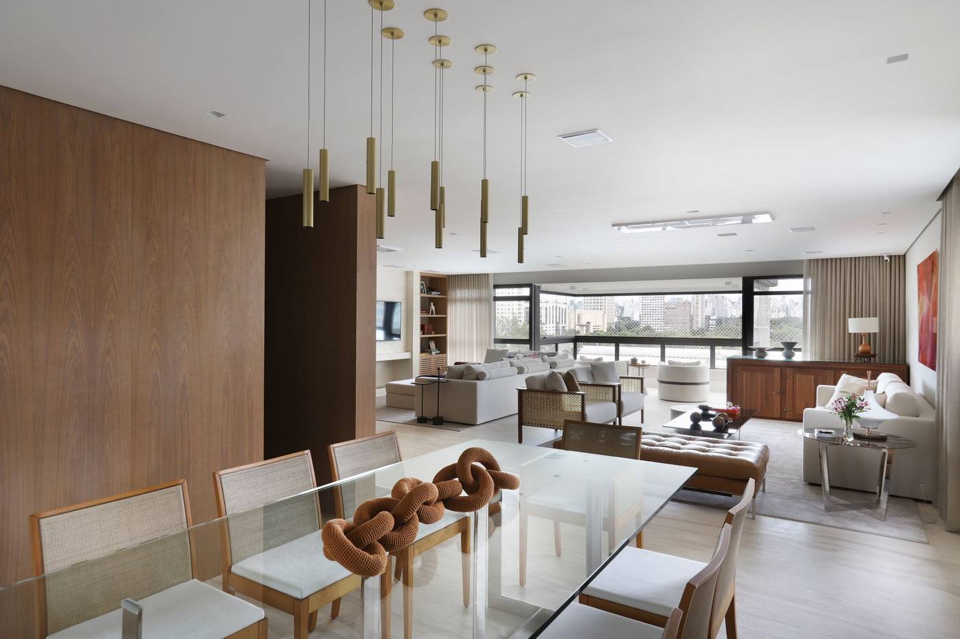 Sala de jantar com painéis de madeira, mesa de vidro e pendentes dourados, em apartamento reformado pela Execcult